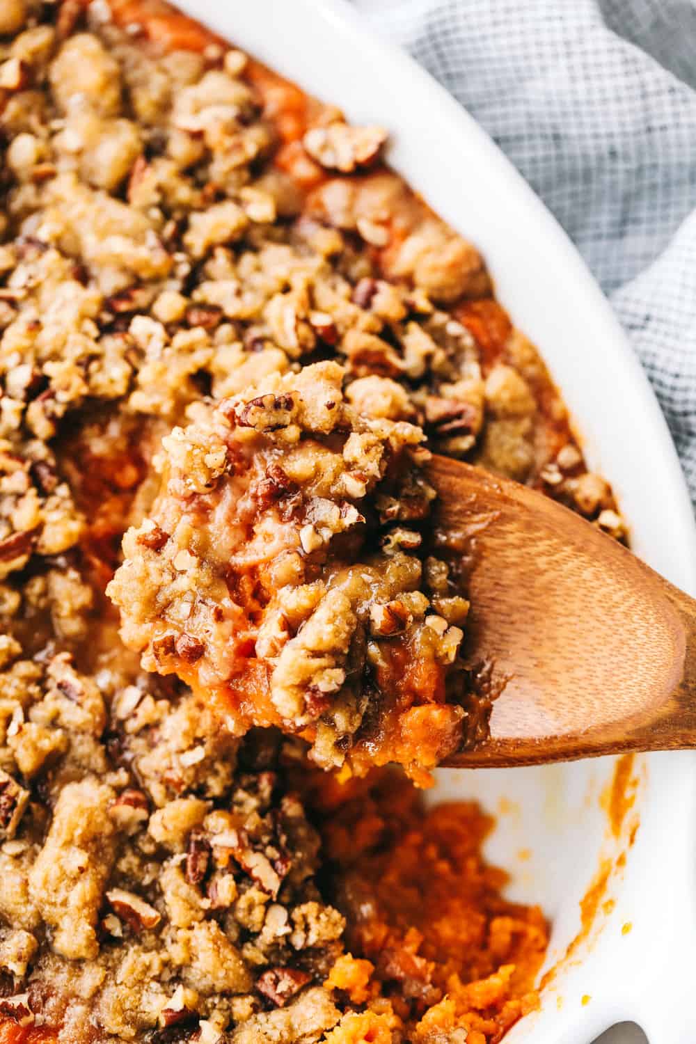 The best sweet potato casserole is smooth and creamy, sprinkled with a brown sugar pecan mixture. It's a sweet and savory side dish that is perfect for the holidays! Taking a scoop of sweet potato casserole with a wooden spoon.