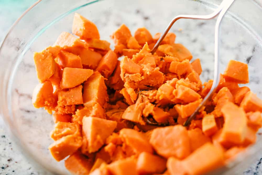 The best sweet potato casserole is smooth and creamy, sprinkled with a brown sugar pecan mixture. It's a sweet and savory side dish that is perfect for the holidays! Mashing sweet potatoes in a clear bowl.