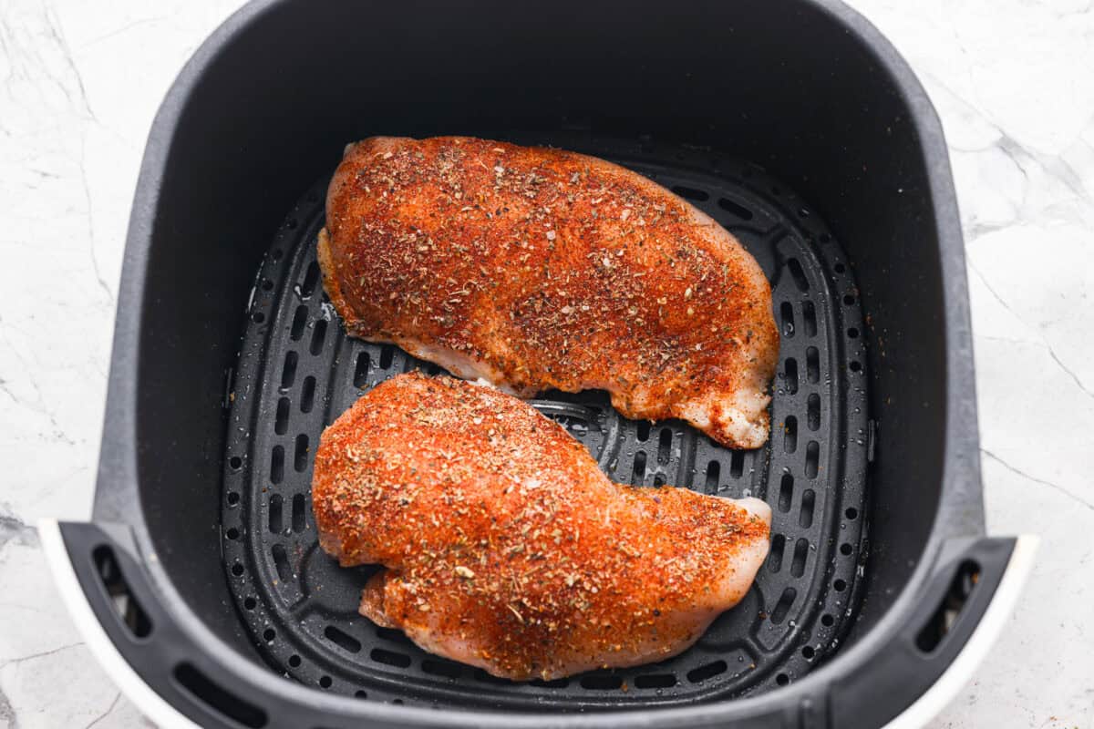 With this Air Fyer Chicken recipe, I am going to show you how to make the most insanely tender and juicy chicken! The secret? The incredible seasonings! They create a nice golden, crispy outside with a juicy, flavor-packed inside! Overhead shot of the seasoned chicken in the air fryer basket.