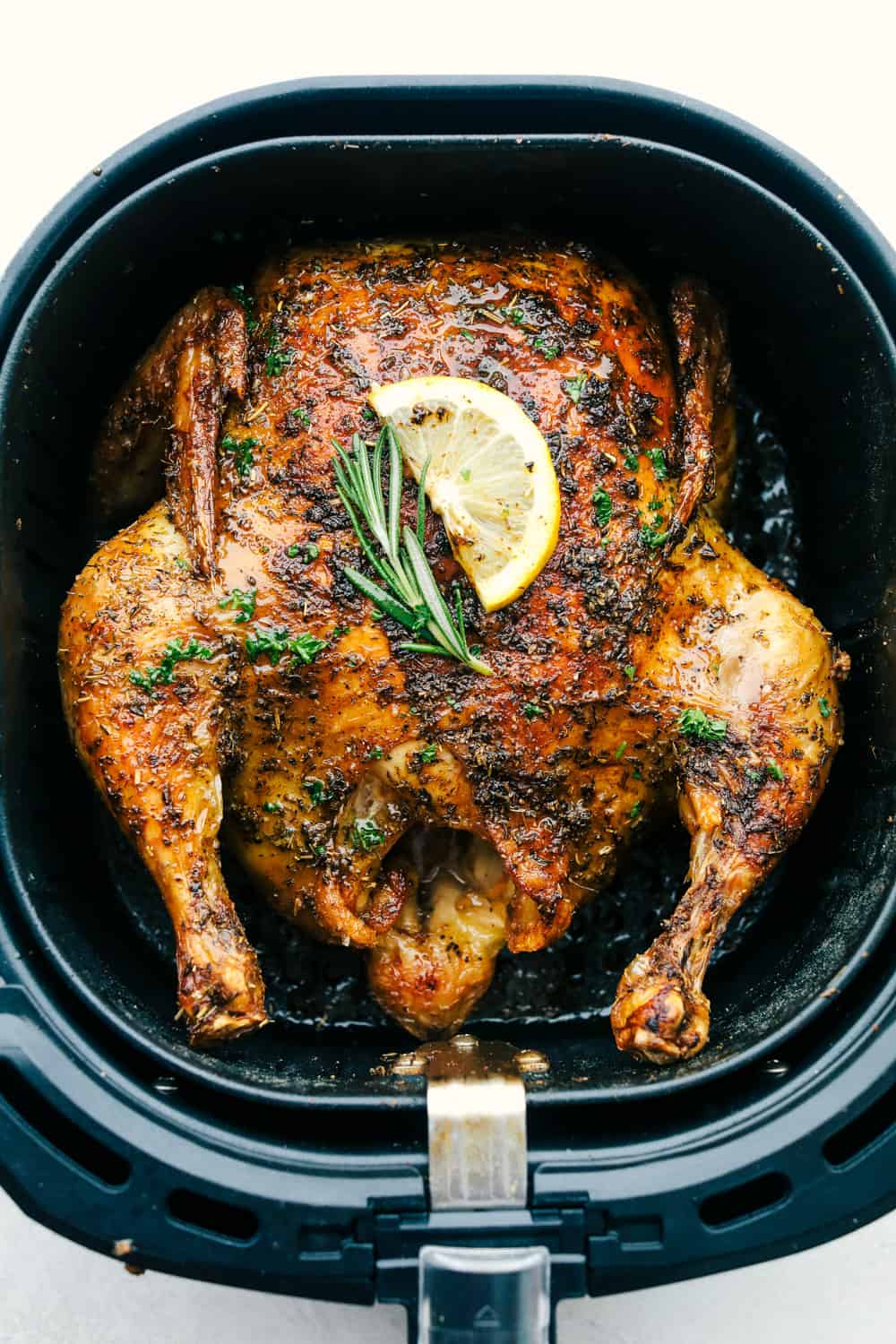 Air Fryer Whole Chicken is going to change the way you do chicken! Super easy, it comes out perfectly tender, juicy and full of flavor! A whole chicken covered with herbs in an air fryer basket.