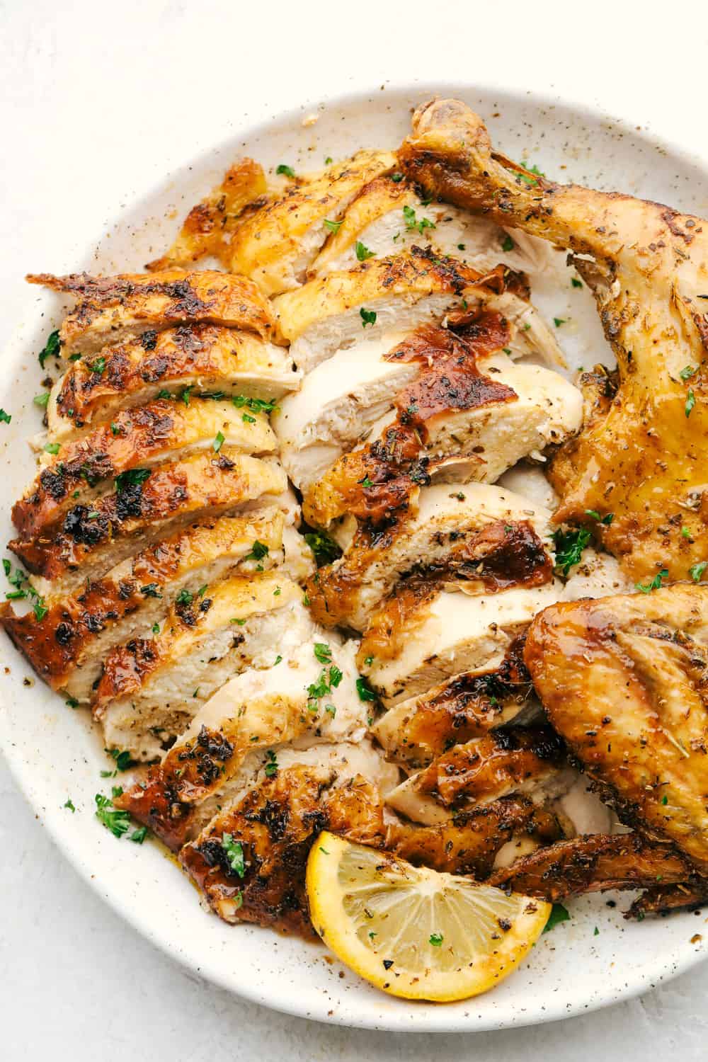 Air Fryer Whole Chicken is going to change the way you do chicken! Super easy, it comes out perfectly tender, juicy and full of flavor! Sliced juicy chicken on a plate with a wedge of lemon.